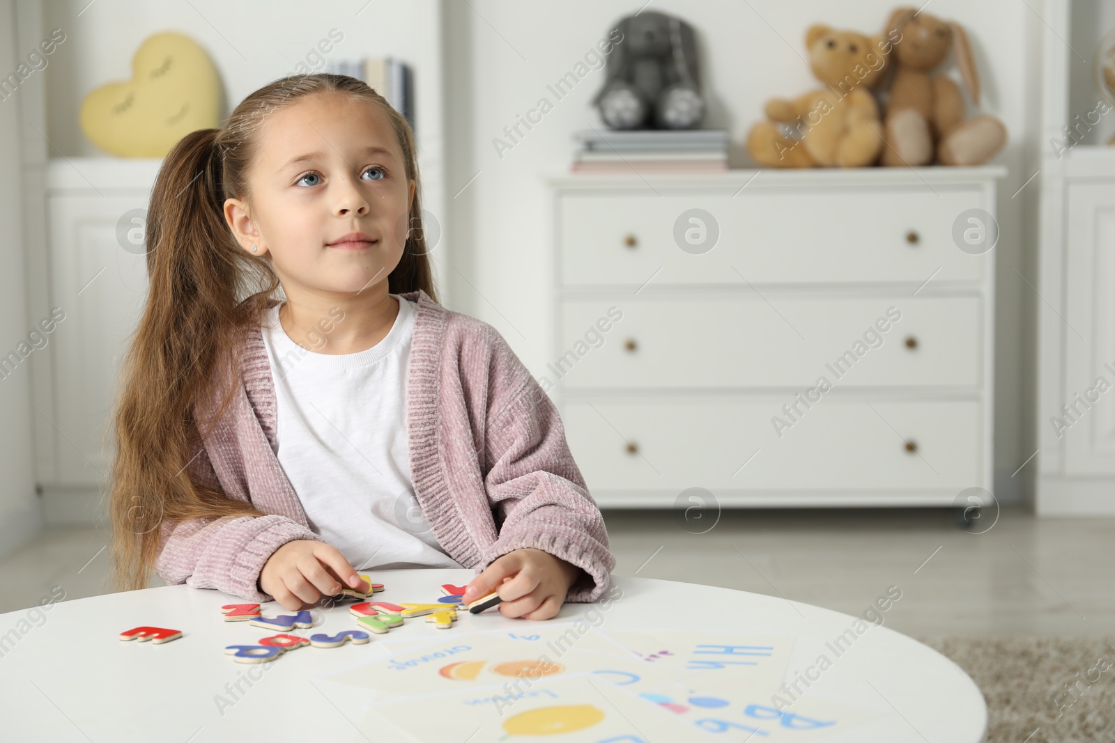 Photo of Little girl learning alphabet with magnetic letters at white table indoors, space for text