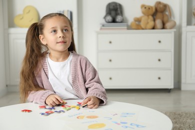 Photo of Little girl learning alphabet with magnetic letters at white table indoors, space for text