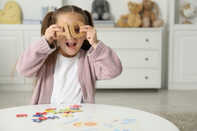 Little girl learning alphabet with different letters at white table indoors