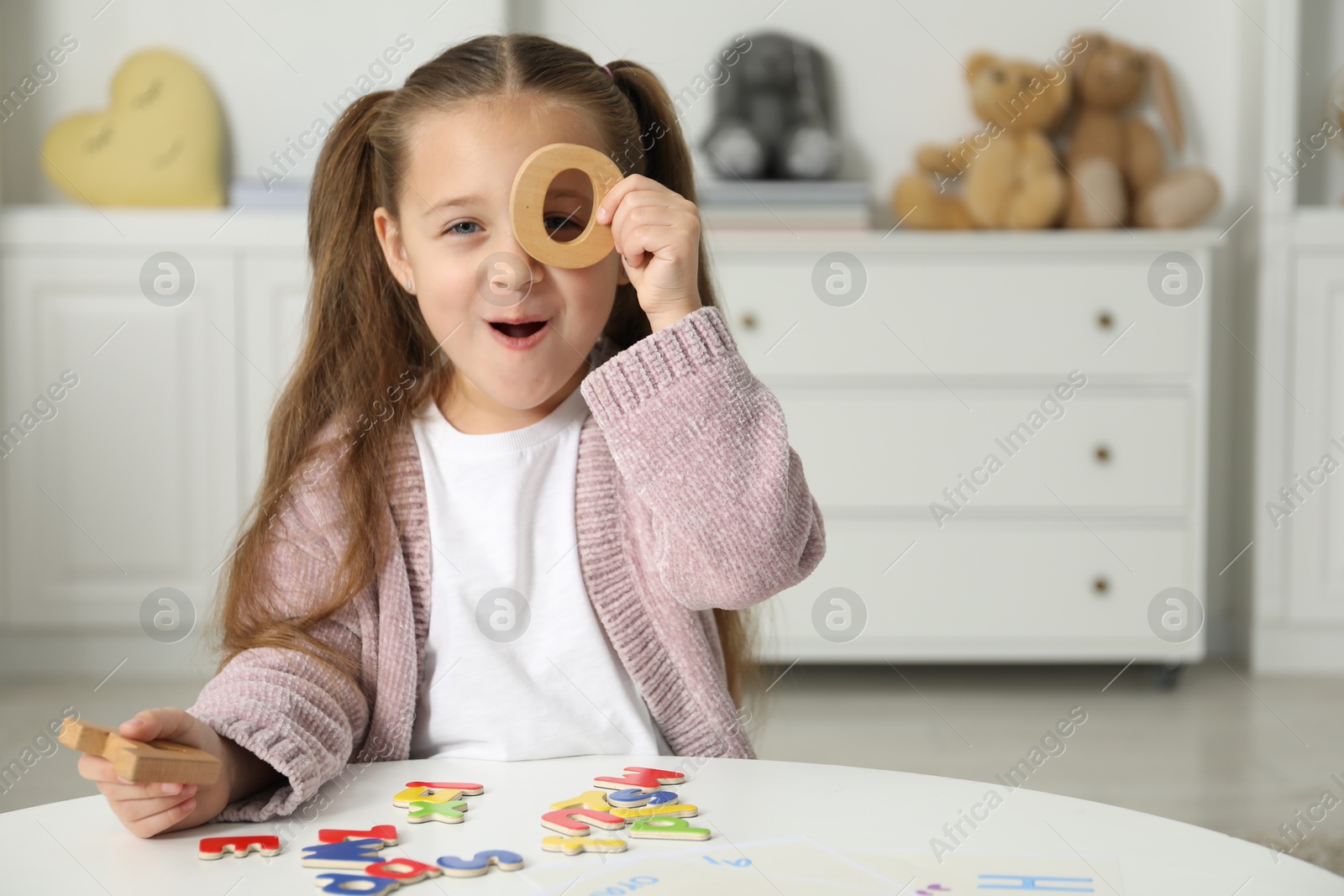 Photo of Little girl learning alphabet with different letters at white table indoors, space for text