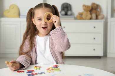 Photo of Little girl learning alphabet with different letters at white table indoors, space for text