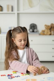 Photo of Little girl learning alphabet with different letters at white table indoors