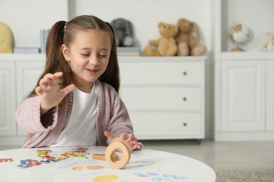 Photo of Little girl learning alphabet with different letters at white table indoors, space for text