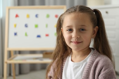 Little girl near board with magnetic letters indoors. Learning alphabet