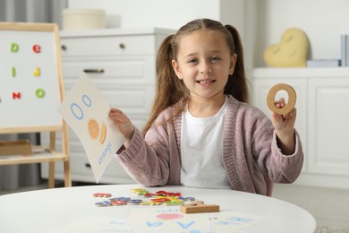 Photo of Little girl learning alphabet with different letters and picture at white table indoors