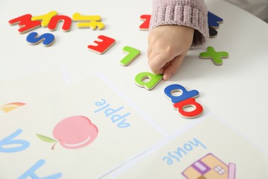 Photo of Little girl learning alphabet with different letters at white table indoors, closeup