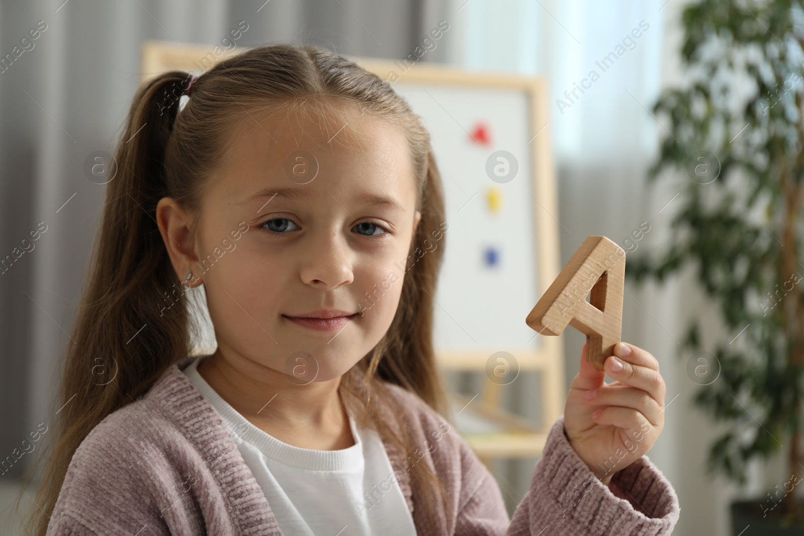 Photo of Learning alphabet. Little girl with wooden letter A indoors