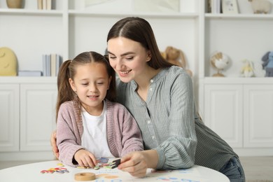 Speech therapist teaching little girl alphabet with different letters at white table indoors