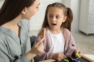 Speech therapist teaching little girl alphabet with different letters indoors