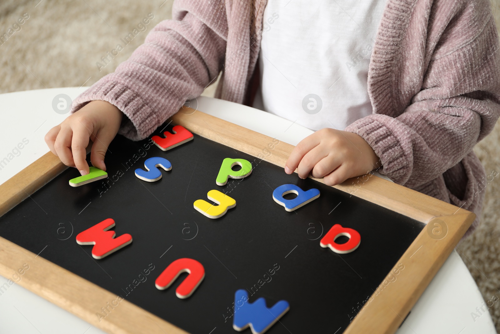 Photo of Little girl learning alphabet with magnetic letters at white table indoors, closeup