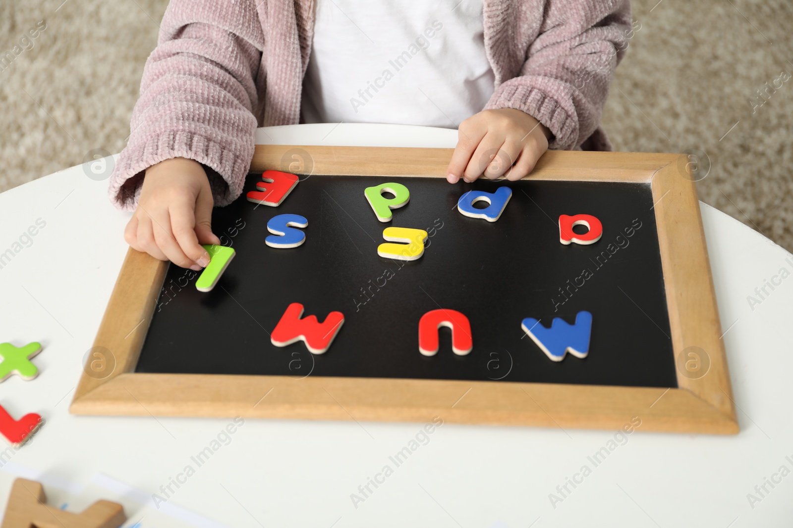 Photo of Little girl learning alphabet with magnetic letters at white table indoors, closeup