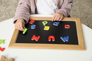 Little girl learning alphabet with magnetic letters at white table indoors, closeup