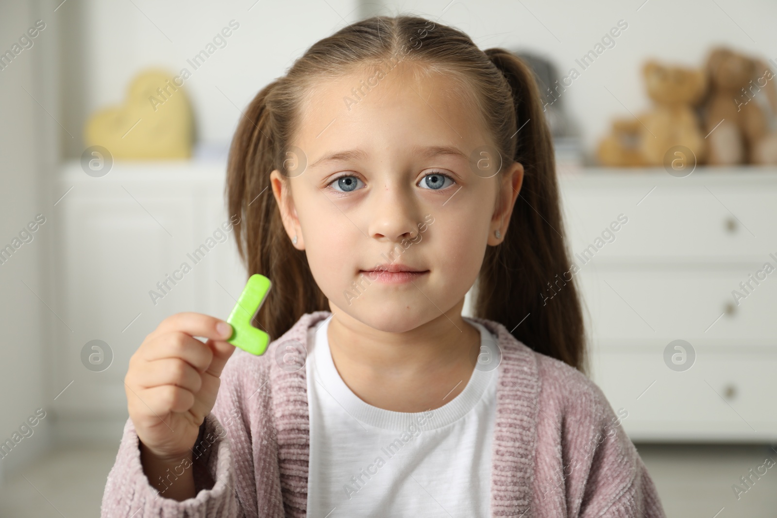 Photo of Learning alphabet. Little girl with green magnetic letter L indoors