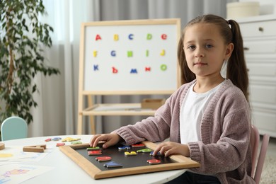 Photo of Little girl learning alphabet with magnetic letters at white table indoors