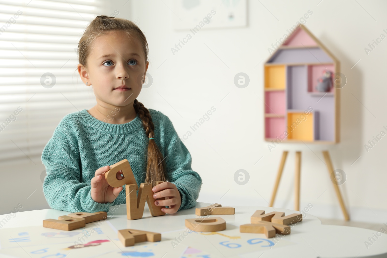 Photo of Little girl learning alphabet with wooden letters at white table indoors