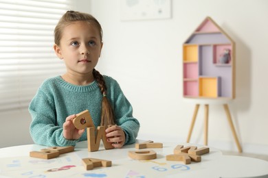 Photo of Little girl learning alphabet with wooden letters at white table indoors