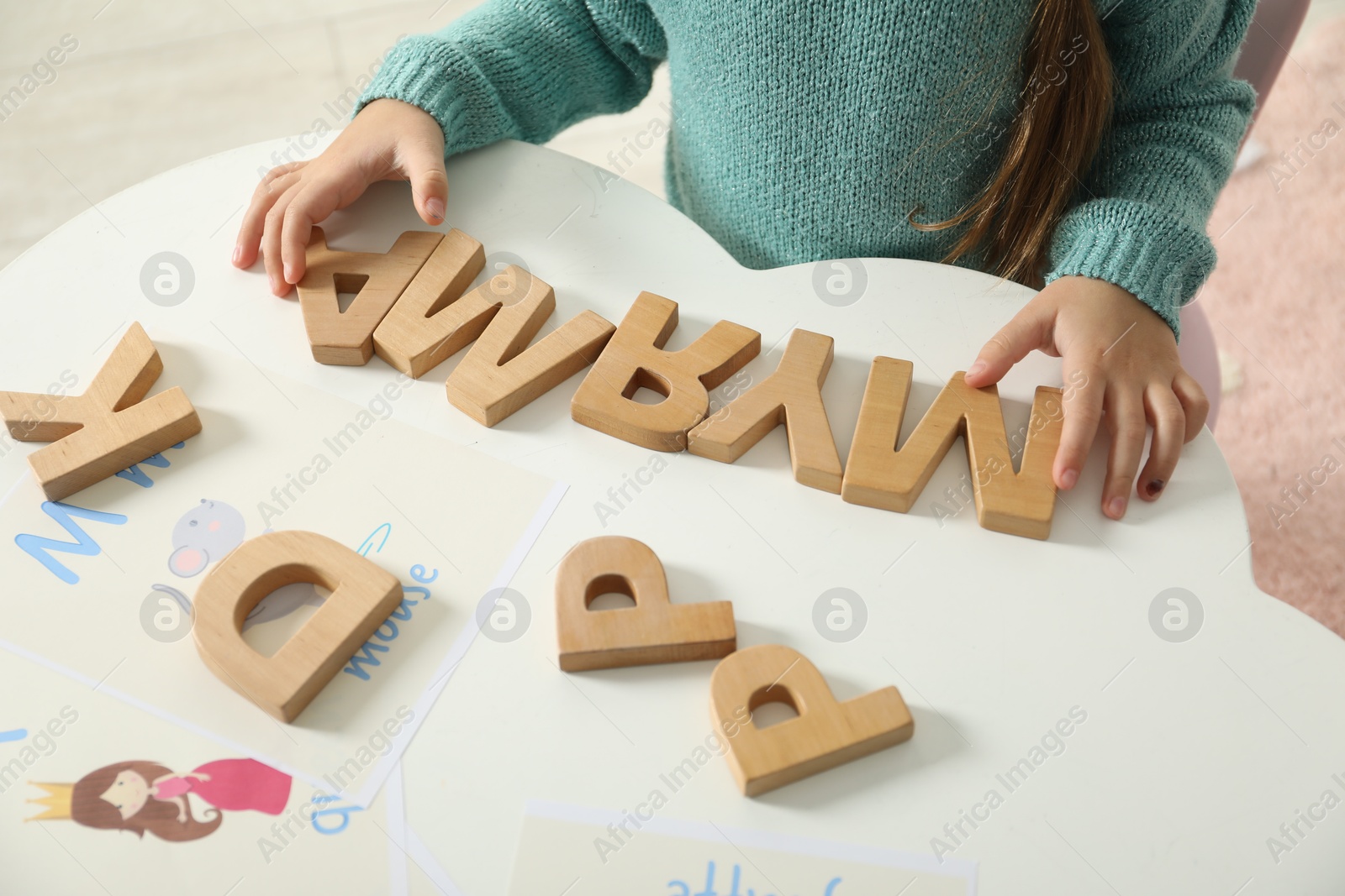 Photo of Little girl learning alphabet with wooden letters at white table indoors, closeup