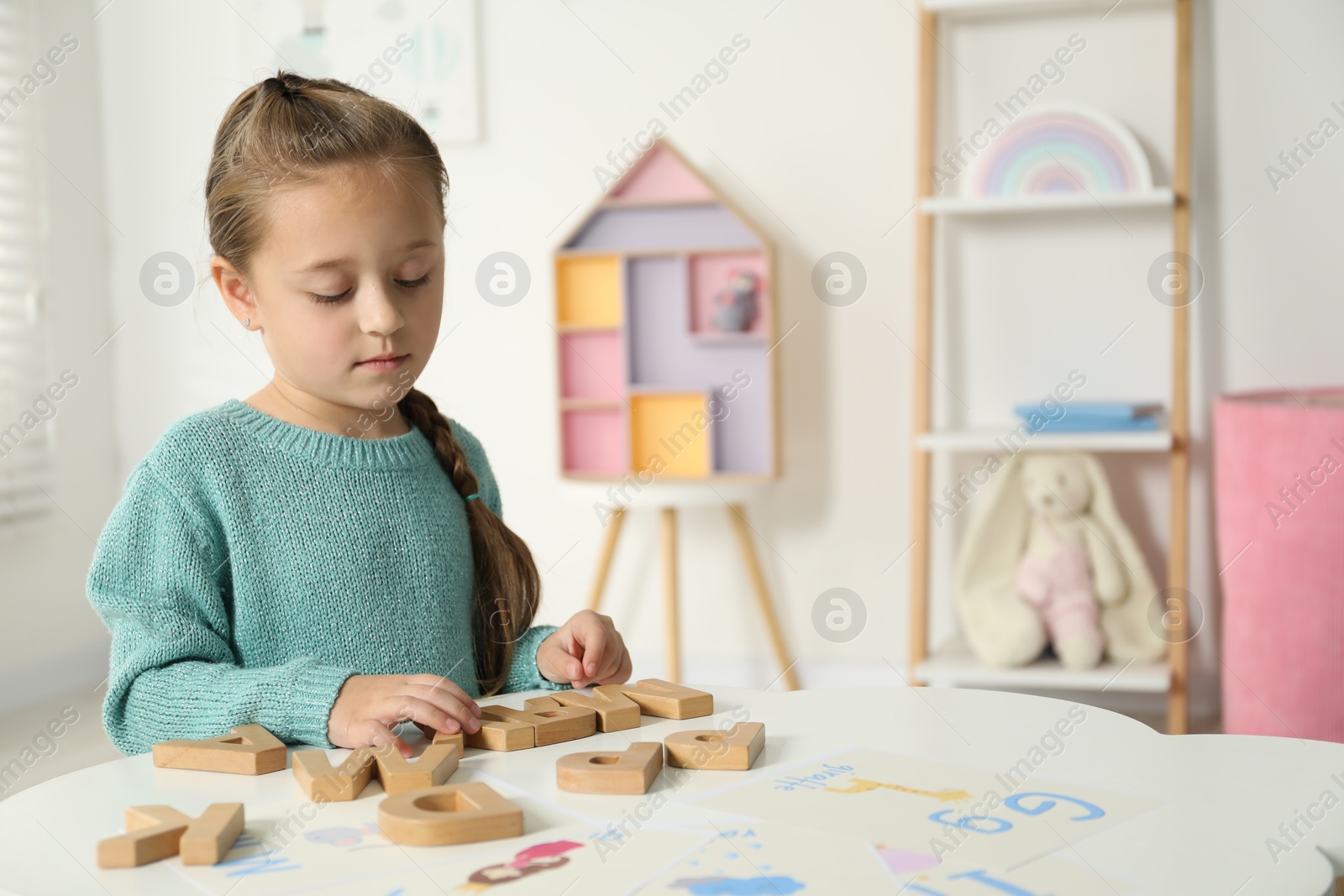 Photo of Little girl learning alphabet with wooden letters at white table indoors