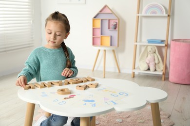 Photo of Little girl learning alphabet with wooden letters at white table indoors