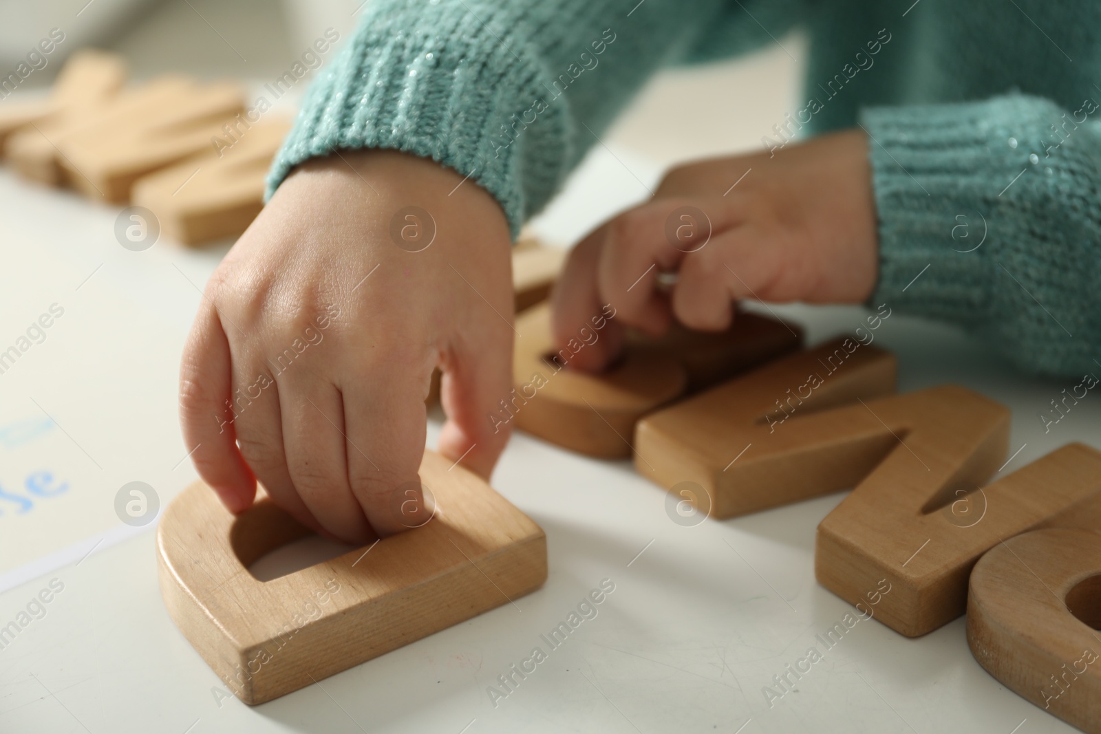 Photo of Little girl learning alphabet with wooden letters at white table indoors, closeup