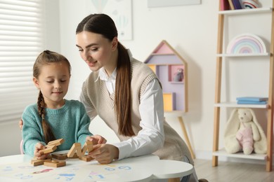 Speech therapist teaching little girl alphabet with wooden letters at white table indoors