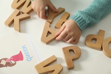 Photo of Little girl learning alphabet with wooden letters at white table indoors, closeup