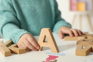 Photo of Little girl learning alphabet with wooden letters at white table indoors, closeup