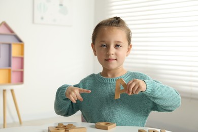 Photo of Learning alphabet. Little girl with wooden letter A at white table indoors