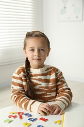 Photo of Little girl learning alphabet with magnetic letters at white table indoors