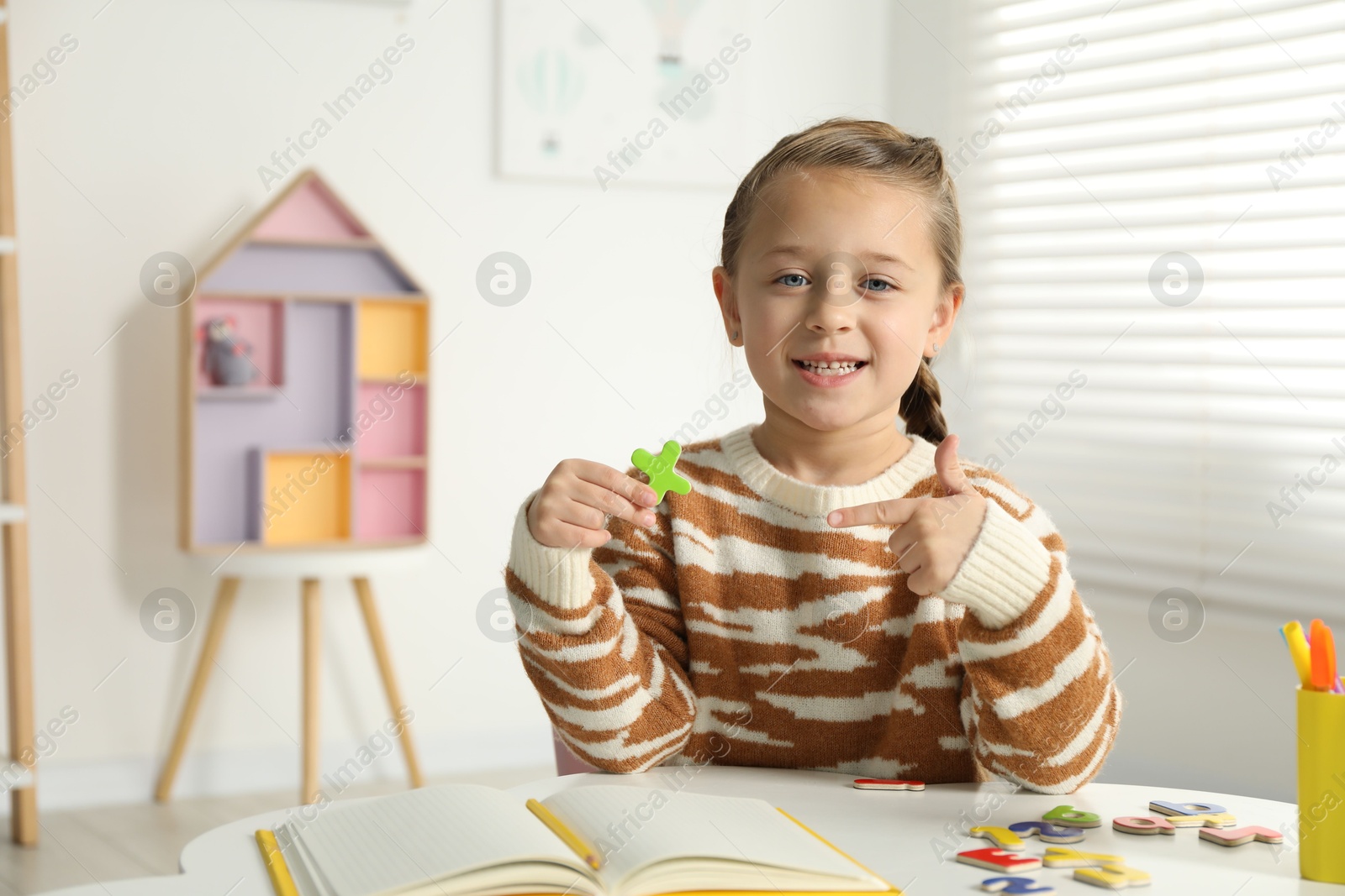 Photo of Little girl learning alphabet with magnetic letters at white table indoors