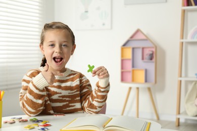 Photo of Little girl learning alphabet with magnetic letters at white table indoors