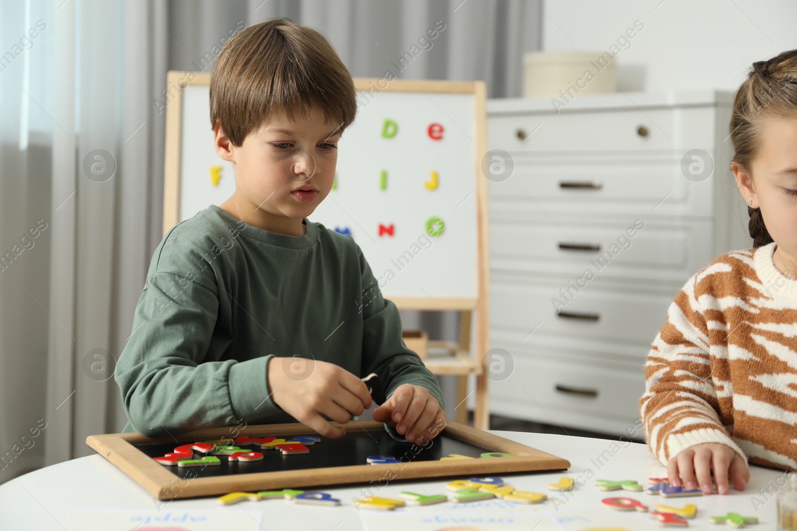 Photo of Little kids learning alphabet with magnetic letters at white table indoors