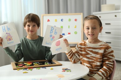 Photo of Little kids learning alphabet with magnetic letters and pictures at white table indoors