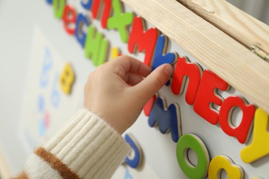 Photo of Little girl learning alphabet with magnetic letters indoors, closeup