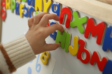 Photo of Little girl learning alphabet with magnetic letters indoors, closeup