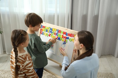 Speech therapist teaching little kids alphabet with magnetic letters indoors