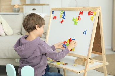 Photo of Little boy learning alphabet with magnetic letters indoors