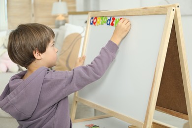 Photo of Little boy learning alphabet with magnetic letters indoors