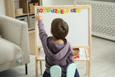 Photo of Little boy learning alphabet with magnetic letters indoors, back view