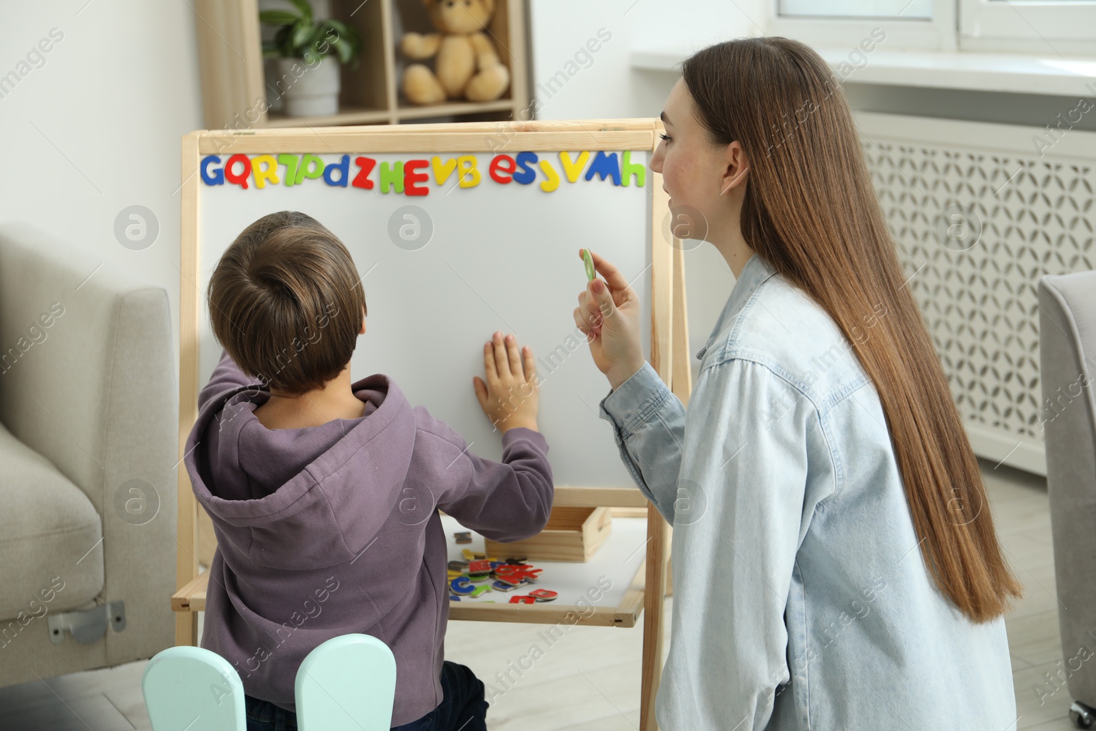 Photo of Speech therapist teaching little boy alphabet with magnetic letters indoors