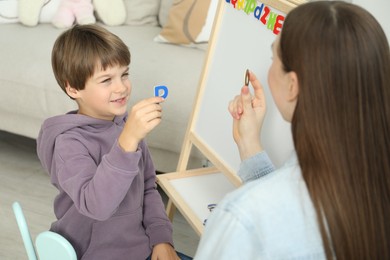 Speech therapist teaching little boy alphabet with magnetic letters indoors