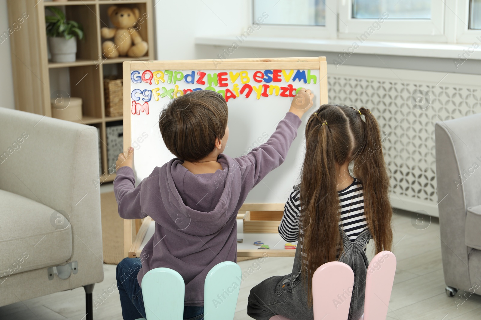 Photo of Little kids learning alphabet with magnetic letters indoors, back view