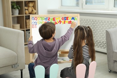 Photo of Little kids learning alphabet with magnetic letters indoors, back view