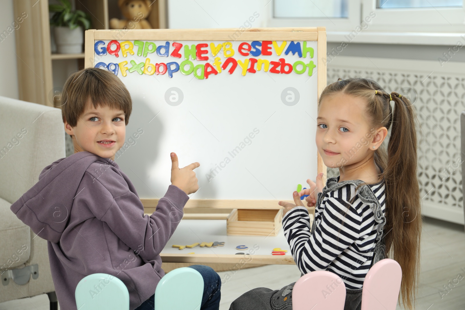 Photo of Little kids learning alphabet with magnetic letters indoors