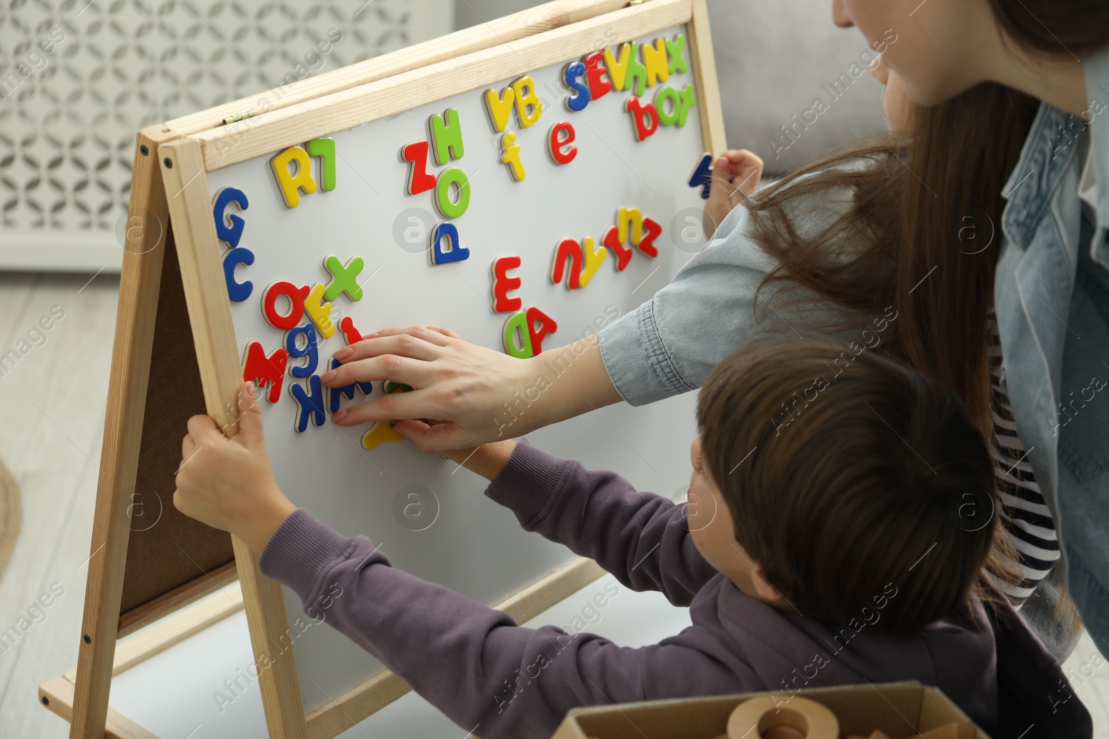 Photo of Speech therapist teaching little kids alphabet with magnetic letters indoors, closeup