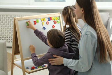 Photo of Speech therapist teaching little kids alphabet with magnetic letters indoors