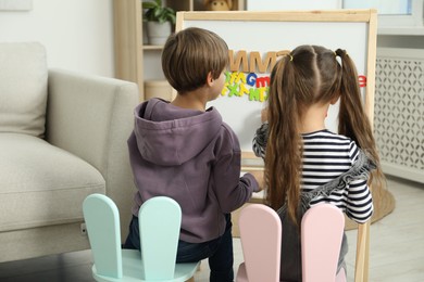 Photo of Little kids learning alphabet with different letters on board indoors, back view