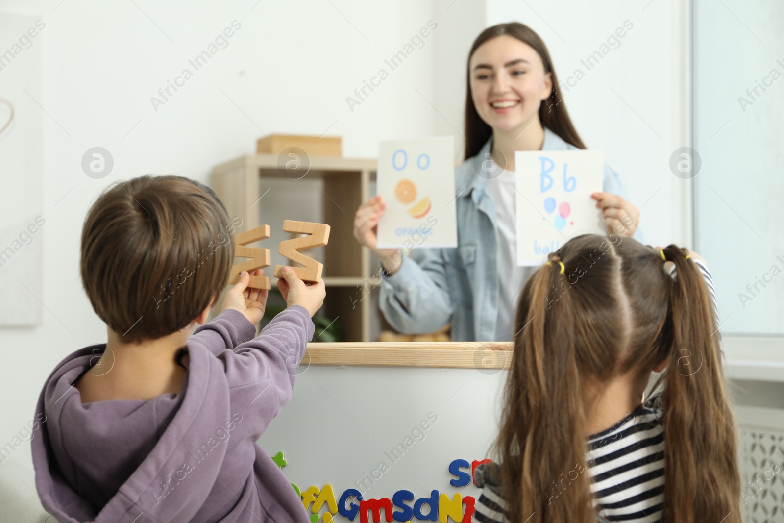 Photo of Speech therapist teaching little kids alphabet indoors, selective focus