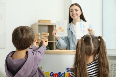 Photo of Speech therapist teaching little kids alphabet indoors, selective focus