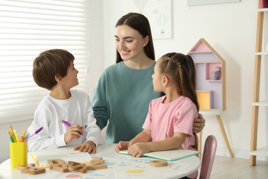 Speech therapist teaching little kids alphabet at white table indoors